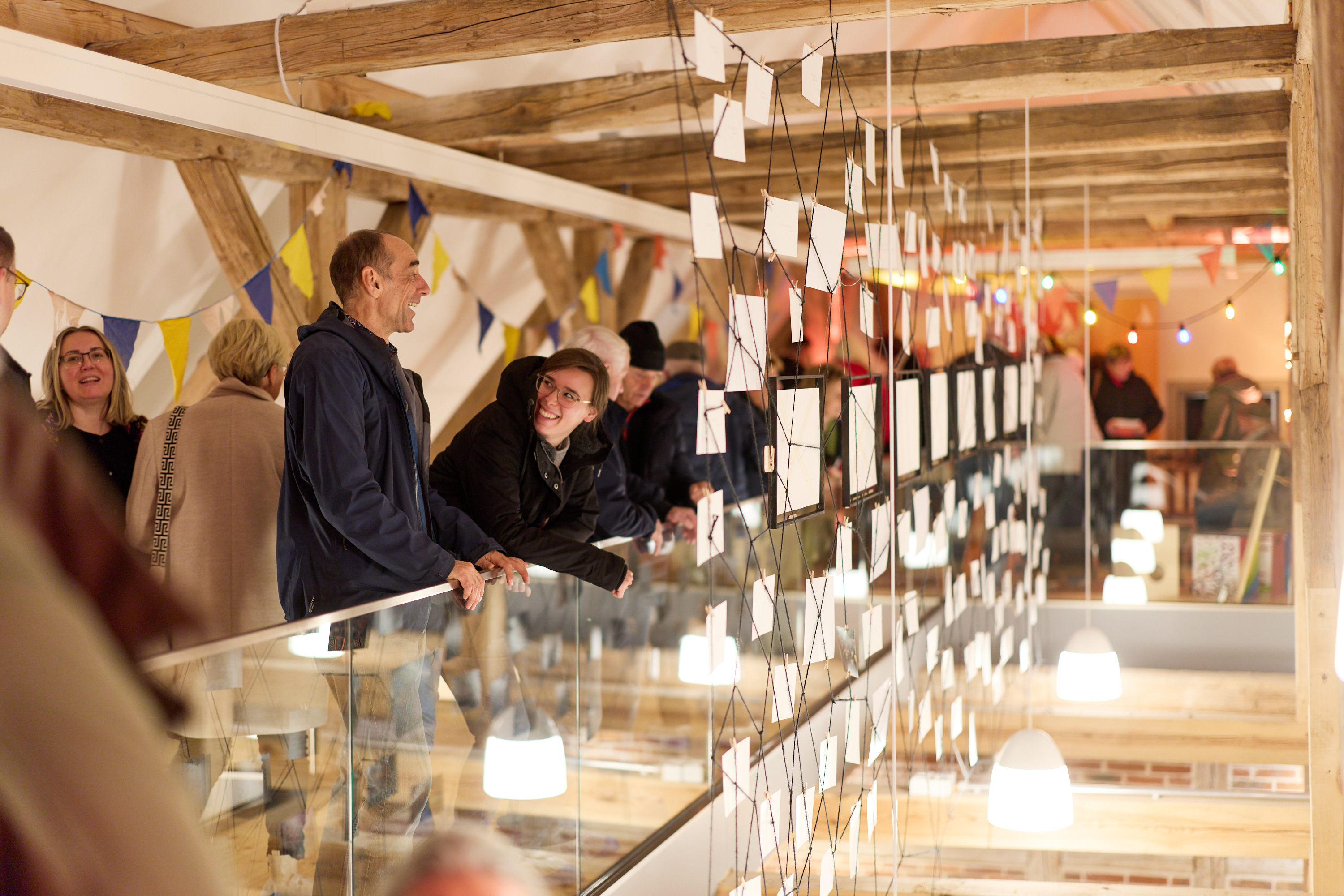 Menschen stehen vor einer Ausstellung von Fotos, die an einem Fadennetz in der Luft hängen