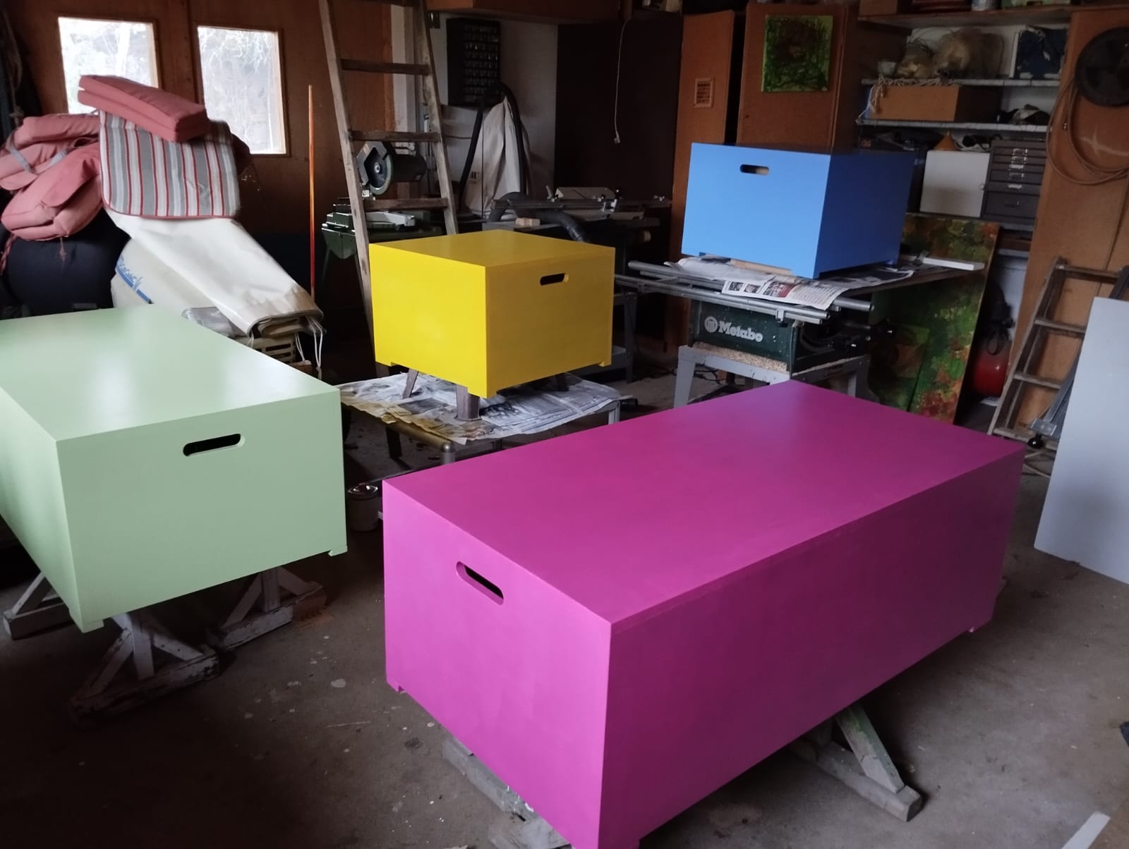 vier bunt bemalte Bänke stehen in einer Werkstatt