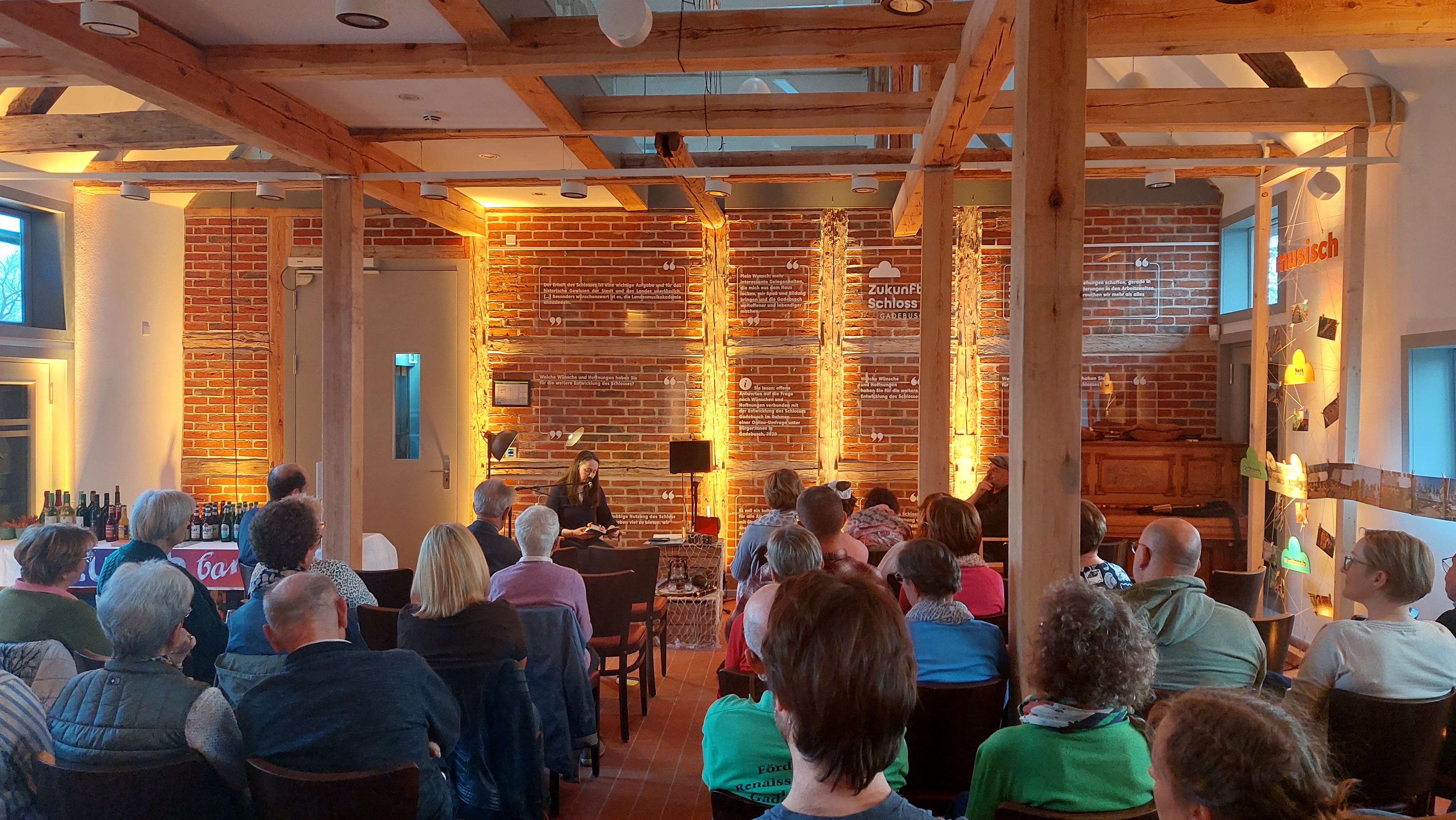 Ein Publikum sitzt in der von innen beleuchteten Remise und lauscht der musikalischen Lesung.